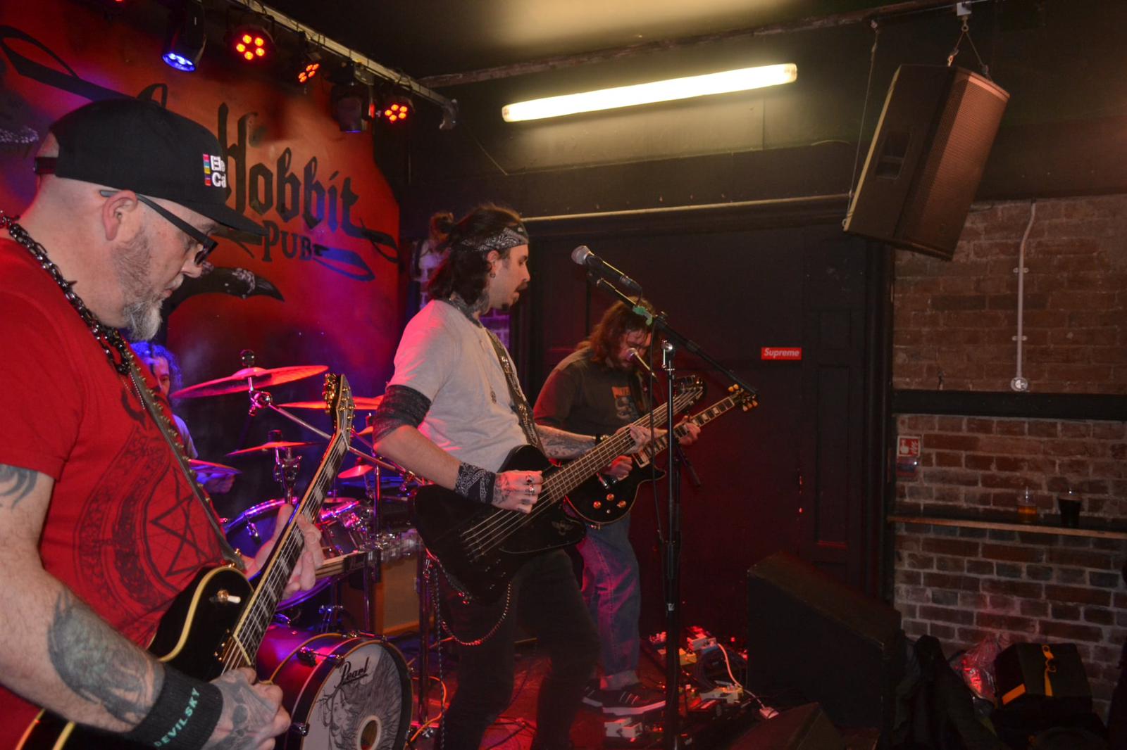 Hexblood performing live at The Hobbit pub, guitarists and drummer under red stage lights