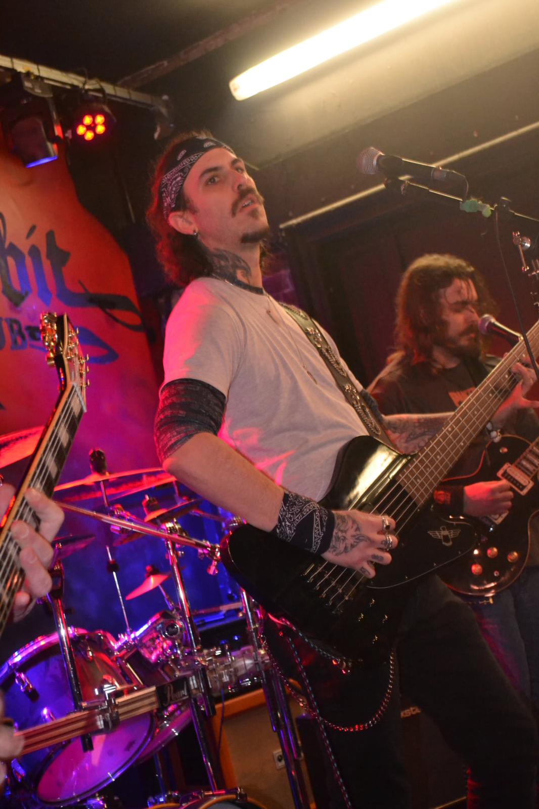 Hexblood bassist singing into the mic with bandmates playing behind him